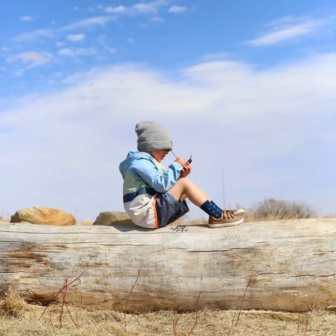 Lifestyle image of child wearing Lamington Children's Arctic Crew Socks while sitting on log.