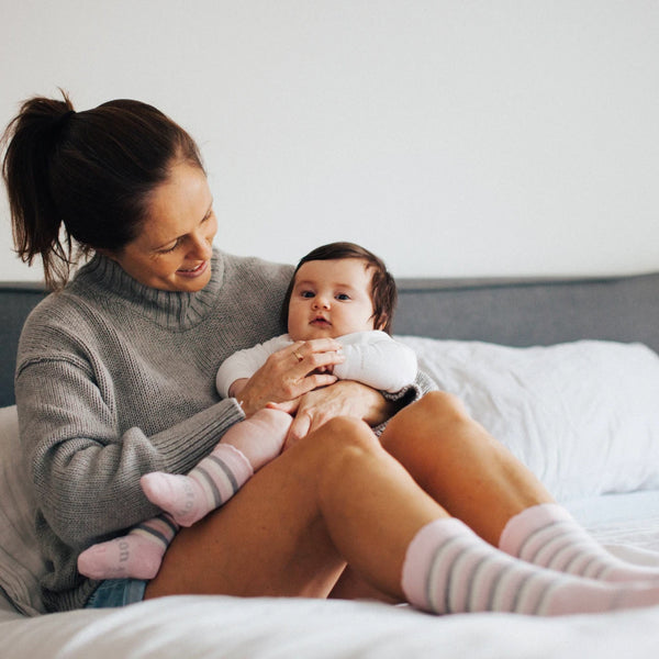 Lifestyle image of baby wearing Lamington Baby & Todder's Fraya Crew Socks while sitting on bed with its mother.