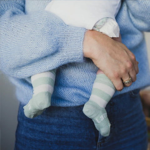 Lifestyle image of baby wearing Lamington Baby & Toddler's Juno Crew Socks while being held by its mother.