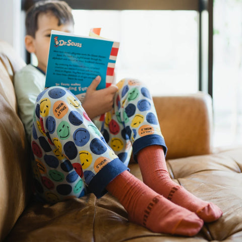 Lifestyle image of child wearing Lamington Children's Brick Crew Socks while sitting on couch in pyjamas reading a Dr Seuss book.
