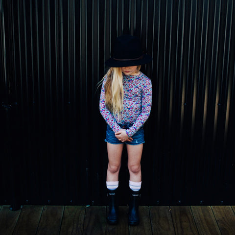 Child wearing Lamington Children's Fraya Crew Socks with boots, standing in front of black corrugated iron wall.