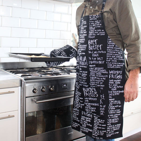 Lifestyle image of model in Moana Road Apron and Mitt Set, Recipe in Black.
